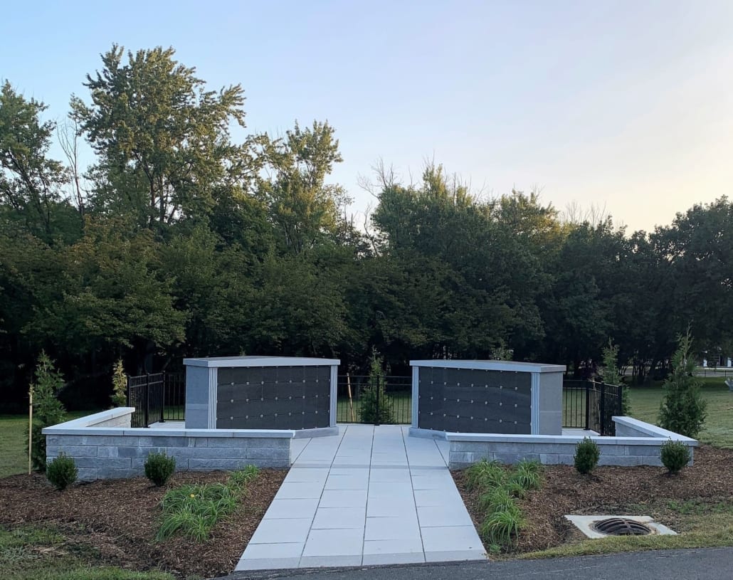 Two granite columbaria with black niche fronts, set behind a low granite wall with a paved walk