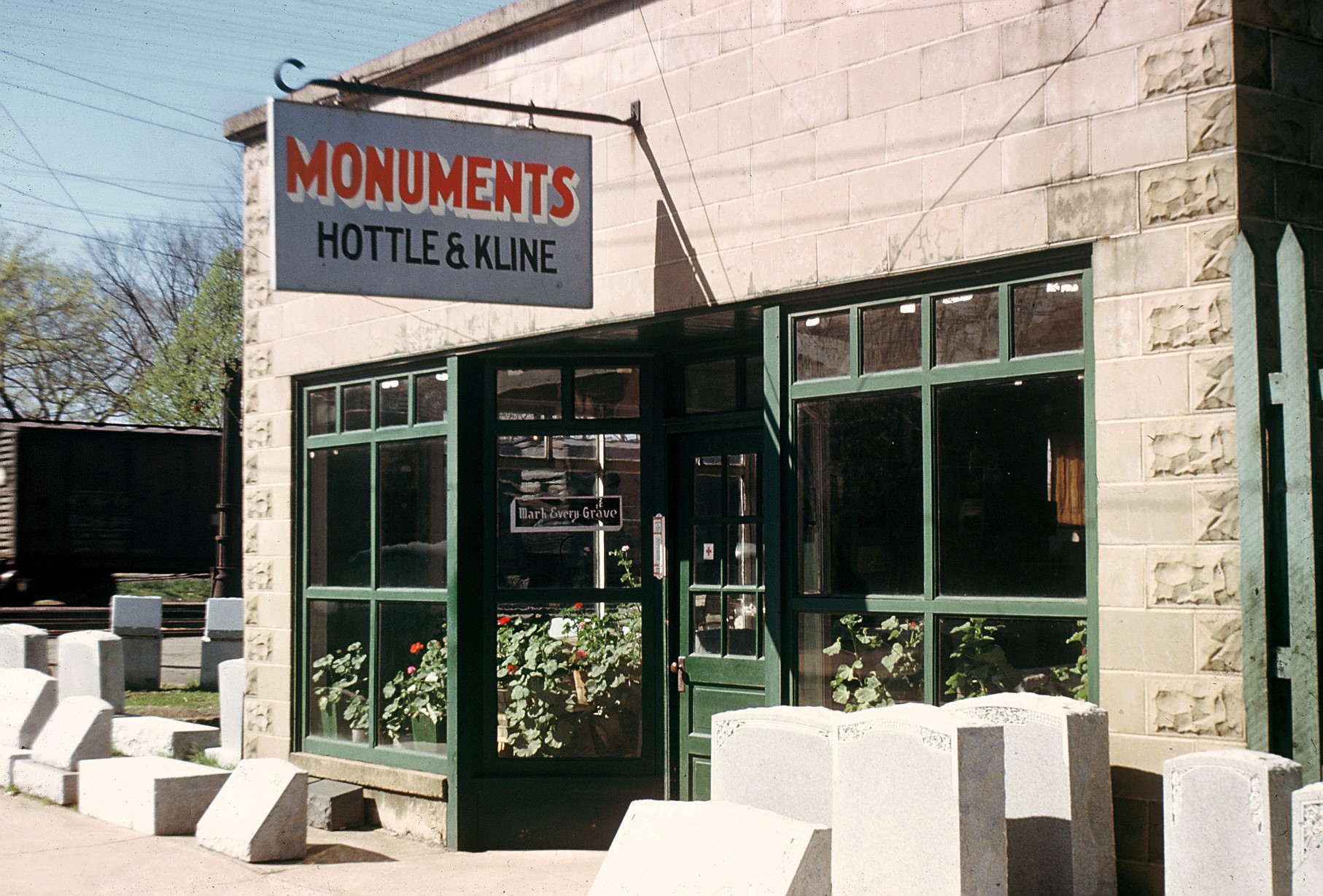 The original Kline shop in Old Town Manassas, with a painted sign reading Monuments, Hottle and Kline, finished headstones on the pavement and a railroad boxcar behind