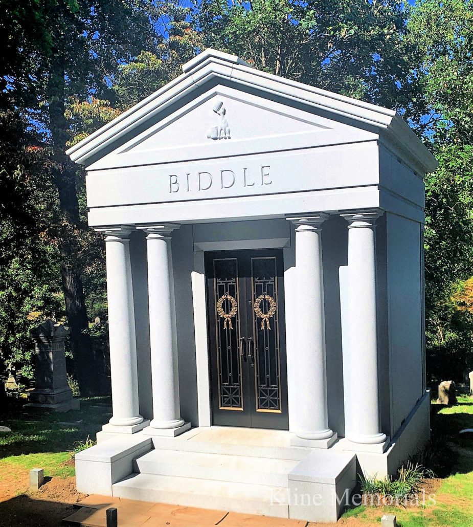 White granite columned mausoleum lettered BIDDLE with bronze doors, standing among trees at Oak Hill Cemetery in Washington DC