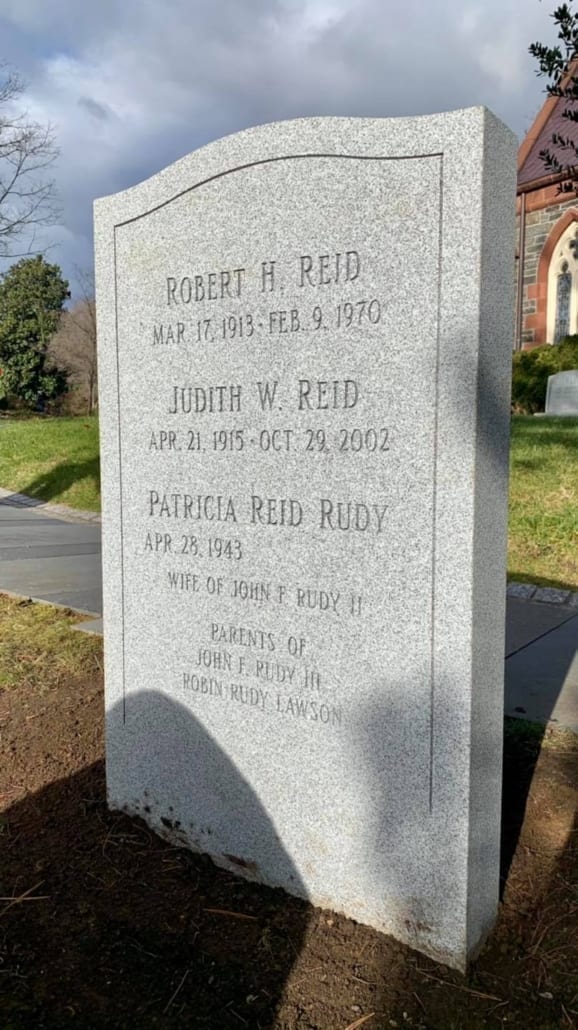 Pale grey granite monolith lettered for three members of the Reid family, with a stone church behind