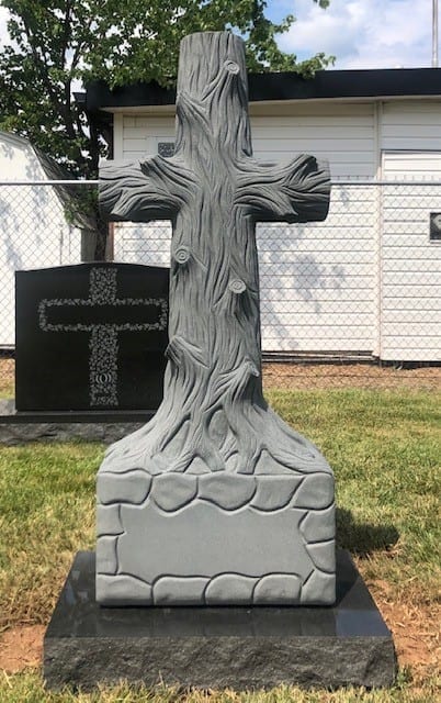 Granite cross carved to look like a tree trunk, standing in the Kline Memorials display yard